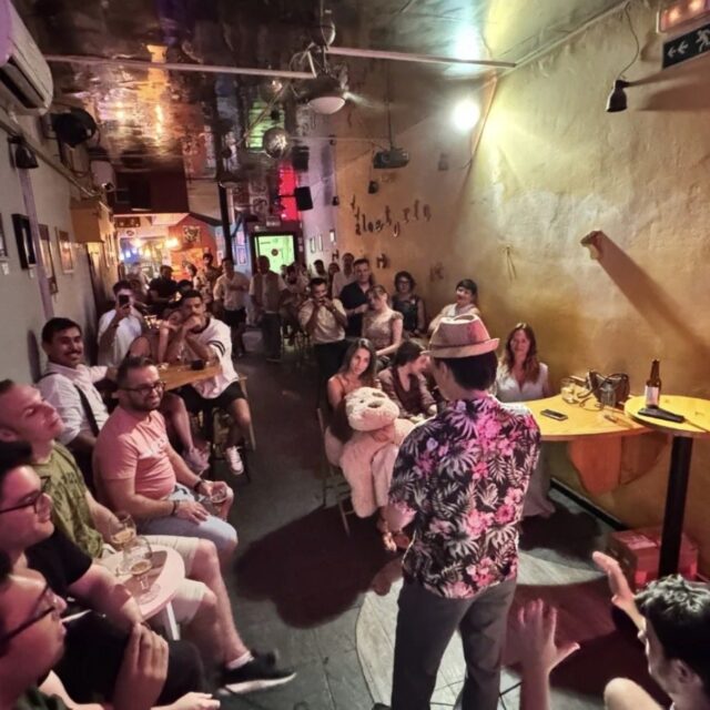 A full room watching a comedian at a No Offense, But... show